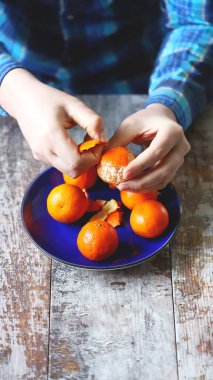 Adamın elleri mandalina soyuyor. Bir tabakta sulu mandalinalar.