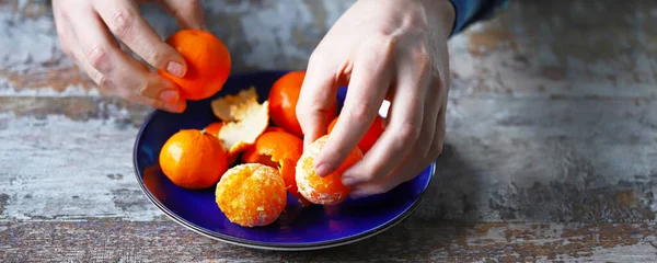 Erkeklerin elleri mandalinayı soyuyor. Tabakta mandalina. Mandalina kabukları.