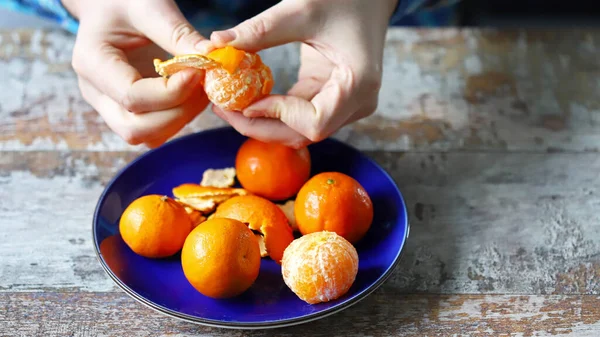 Peeling tangerines. Men\'s hands are peeling mandarin. Tangerines in a plate.