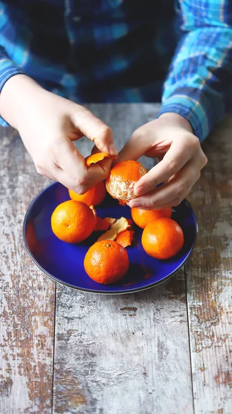 Adamın elleri mandalina soyuyor. Bir tabakta sulu mandalinalar.