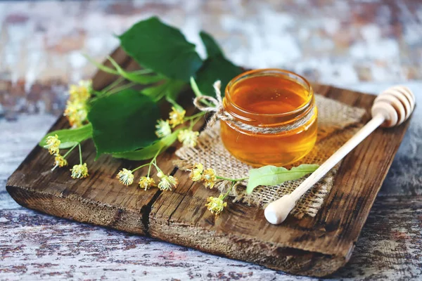 Stick for honey with linden honey. Linden honey in a jar. Leaves and flowers of linden. Summer fresh honey.