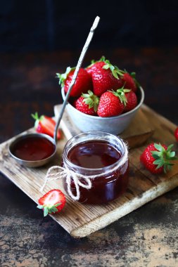 Kavanozda çilek reçeli ve koyu bir yüzeyde taze çilek..