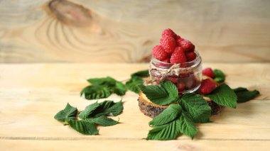 Ahşap bir yüzeyde ahududu ve ahududu yapraklı kavanoz..