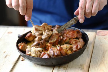 Şef kızartma tavasında kızarmış et parçaları karıştırır. Tavada domuz şişi..