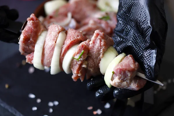 バーベキュー料理 串に手袋をして肉片をシェフによじれている 黒い背景に生のケバブ — ストック写真