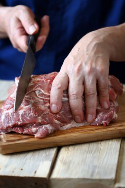Bıçaklı erkek eller tahtada çiğ et kesiyor. Aşçı çiğ et kesiyor..