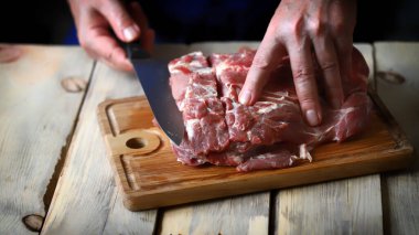 Bıçaklı erkek eller tahtada çiğ et kesiyor. Aşçı çiğ et kesiyor..