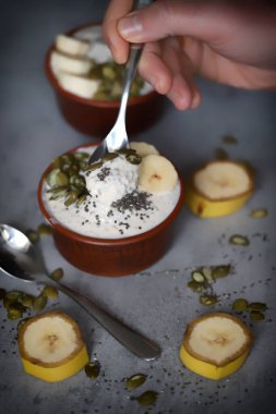 Bir kaşık yoğurtla erkek eli. Tohumlu ve muzlu sağlıklı chia yoğurdu..
