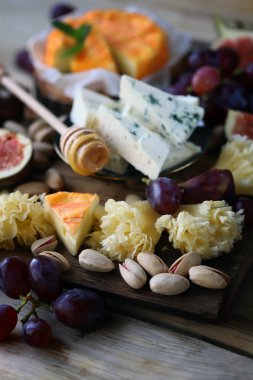 Üzümlü peynir tahtası, incir, fıstık ve bal. Tahtada meyveli farklı peynir türleri.