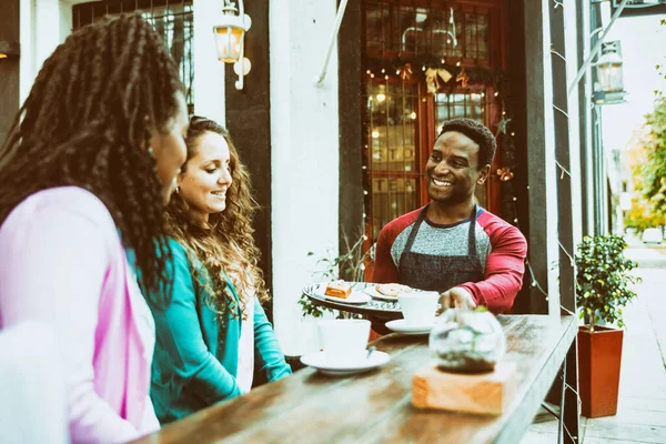 Young waiter serves two cute women.