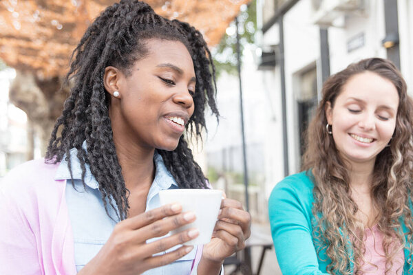 Working meeting between two young women in front of a cafe, with laptop and mobile.