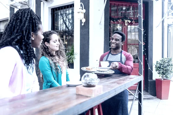 Young waiter serves two cute women.