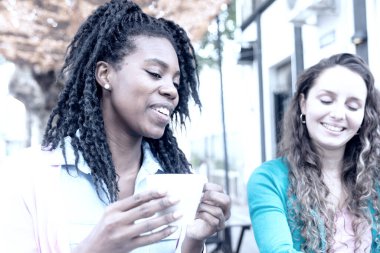 Kahve fincanı ve beyaz bir kadının yanında oturan gülümseyen Afrikalı kadın.