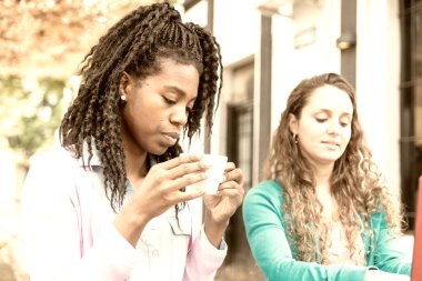 Kahve fincanı ve yanında beyaz bir kadın oturan Afrikalı genç bir kadın.