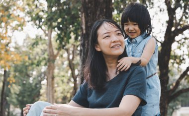 Asyalı küçük kız parkta gülümseyerek annesine sarılıyor. Aile ilişkisi ve rahatlama zamanı kavramı.