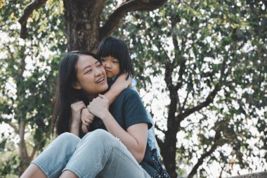 Asyalı küçük kız parkta gülümseyerek annesine sarılıyor. Aile ilişkisi ve rahatlama zamanı kavramı.