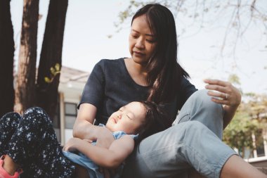 Asyalı küçük kız parkta annesinin bacaklarının üzerinde uyuyor. Aile ilişkisi ve rahatlama zamanı kavramı.