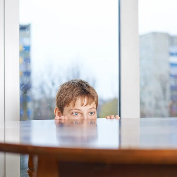Boy peeking out from the wooden desk table — Stock Photo, Image
