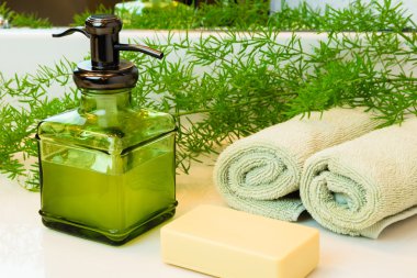 Yeşil cam şişe sıvı Arap sabunu ile pompa. Bej bar sabun. Yeşil havlu bir spa ortamda haddelenmiş. Yeşil bitki dekor içinde geçmiş. Beyaz Banyo tezgah.