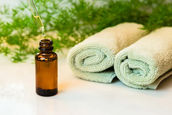 Bottle with essential oil, towels and greens on bathroom counter Stock Photo