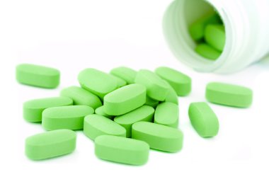 Açık ilaç kavanoz ve yeşil multi-vitamin hapları bir yığın.