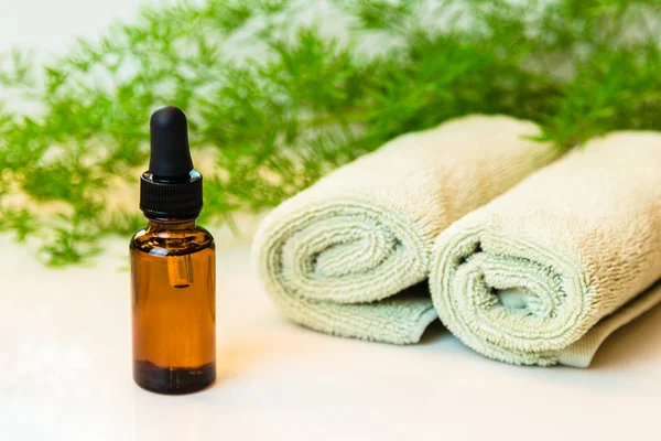 Bottle with essential oil, towels and greens on bathroom counter — Stock Photo, Image