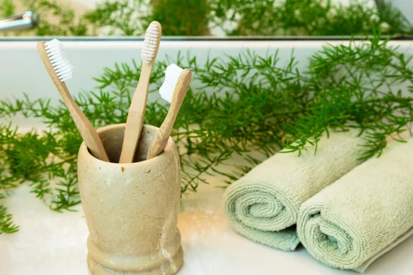 Bamboo toothbrushes in cup, towels and greens on bathroom counte Royalty Free Stock Photos