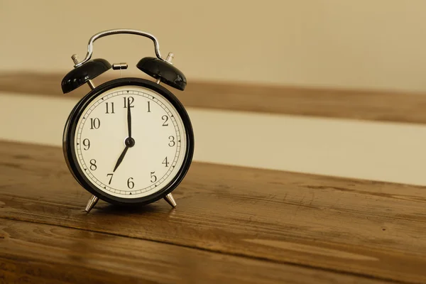 Vintage alarm clock on rustic wood table. Shows 7 o'clock. Stock Photo