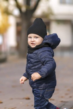 Siyah şapkalı küçük çocuk kameraya bakıyor. Sonbahar şehrinin arka planındaki çocuk