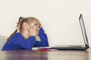 Little girl sitting thinking at the computer. The child dreamed of something during distance learning on the computer