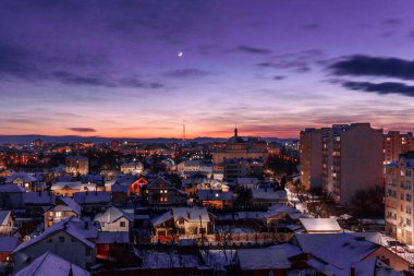 Kış akşamı şehri manzarası. Aydınlanmış şehrin üzerinde ay ve bulutlar