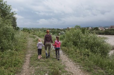 Anne ve iki kızı nehir kenarında yürüyorlar. Aile fırtınadan önce yürür