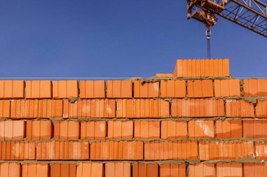 Mavi gökyüzünün arka planında bir tuğla duvar parçası. Tuğla duvar ve kule vinci arkasında