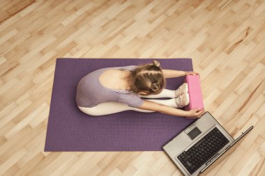 Mor taytlı küçük kız mor bir hasırın üzerinde geriliyor. Çocuk evde bilgisayarın önünde antrenman yapıyor.