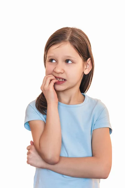 The little girl bites her nails and looks away. The child holds her fingers in her mouth and is worried