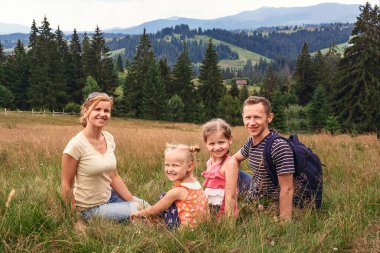 Dağlardaki çimlerin üzerinde oturan genç bir aile. Bir adam, bir kadın ve iki kızı bir sırt çantasıyla dağlara seyahat ediyor.