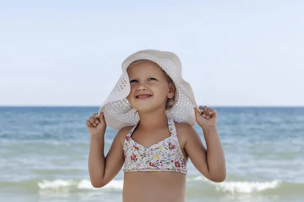 穿着泳衣 戴着白帽子的小女孩躺在海面上 海滩上的一个孩子摆姿势要相机看 — 图库照片