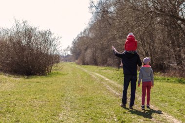 Doğada yürüyen iki kızı olan genç bir baba. İki çocuklu bir adam patikada yürüyor, dikiz aynasından. Babam bebeği omuzlarında taşıyor..