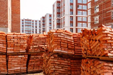 Yüksek binaların arka planında paletler dolusu tuğla var. Evin yanında tuğla yığını ve iskelesi olan inşaat alanı.