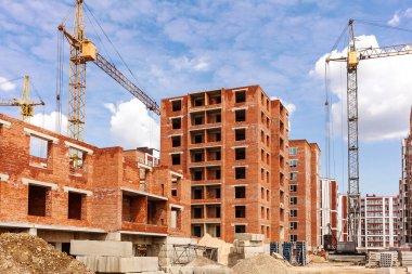 Construction site of a brick high-rise building. Tower crane near high-rise building on background of cloudy sky. 