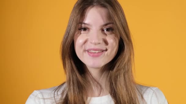 Retrato de una joven feliz sonriendo tímidamente, su boca mirando a la cámara sobre un fondo anaranjado aislado. Movimiento lento — Vídeos de Stock