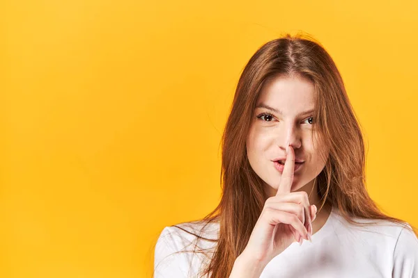 Portrait young girl, showing silence with finger touching lips. Isolated over bright vivid yellow background