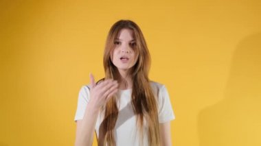 Güzel bir genç kadın, sarı arka planda tek başına dikilirken kameraya öpücük yolluyor.