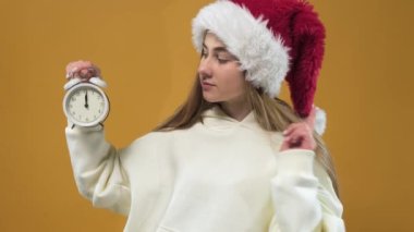 Good morning, woman. The girl is holding an alarm clock on an orange background. The concept of Christmas.