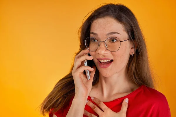 Retrato de hermosa linda mujer joven vestida con camisa roja sosteniendo teléfono cerca de las conversaciones de oído — Foto de Stock