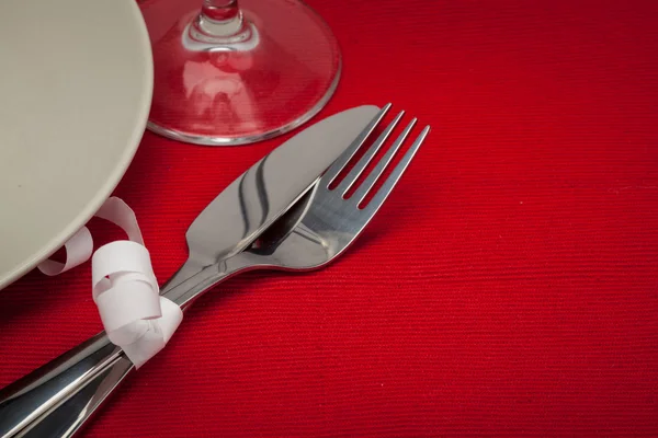 Kniv, glas, vit platta och gaffel på rött — Stockfoto