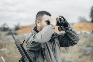 Tüfekli bir adam dürbünle bakıyor. Özel askeri müteahhit ya da avcı
