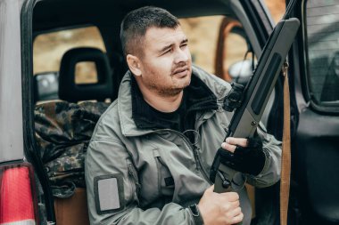 Bir off-road arabasının bagajında tüfekli bir adam. Özel askeri müteahhit ya da avcı