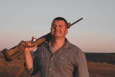 Orta yaşlı, ekose gömlekli, tüfekli orta yaşlı, ekose gömlekli, alacakaranlık saçlı bir adam..