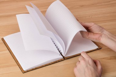 Bir adam sayfaları açık bir not defterinde beyaz sayfalar ve tahta kahverengi bir kutuya bağlanmış bir şekilde masanın üzerinde duruyor.